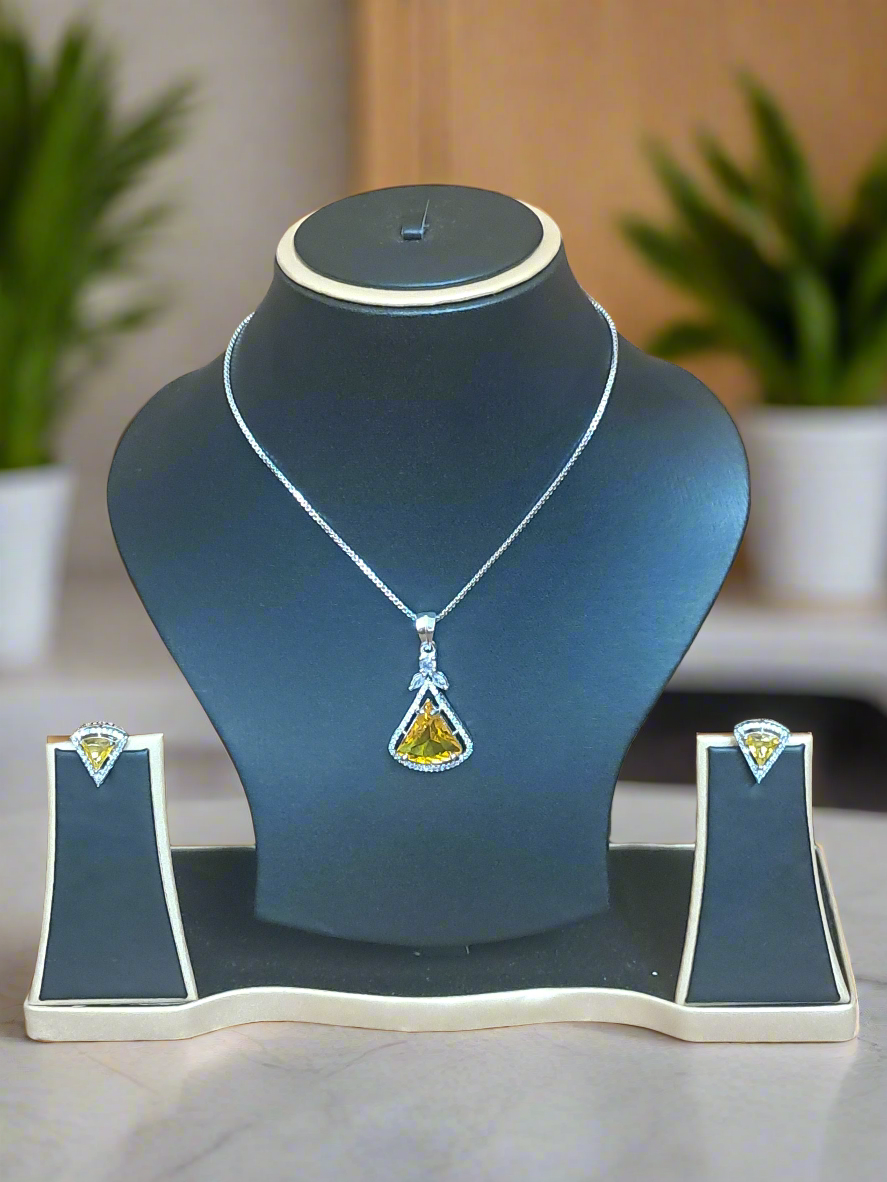 background-editor_output_36fc95c9-46fc-49b7-a725-f8be30d900cf Aqua yellow CZ studded pendant set displayed on a black jewelry stand, featuring a silver-plated chain and matching earrings by Garimas.