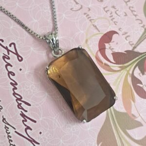 Garimas Smoky Yellow pendant with silver chain, set against a patterned background.