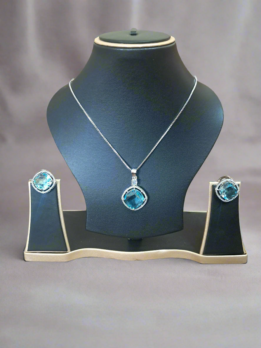 background-editor_output_0396b389-11e2-4f7d-8ea2-2a18bf3d3de8-1 Aqua Blue Pendant Set with CZ studs and silver-plated chain displayed elegantly on a black jewelry stand.