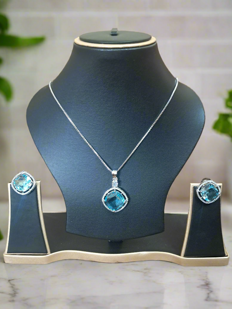 background-editor_output_4ffdeb53-a1eb-4139-b07b-f86d242d58ee-1 Aqua Blue Pendant Set by Garimas featuring CZ studs and silver-plated chain displayed on a jewelry stand.
