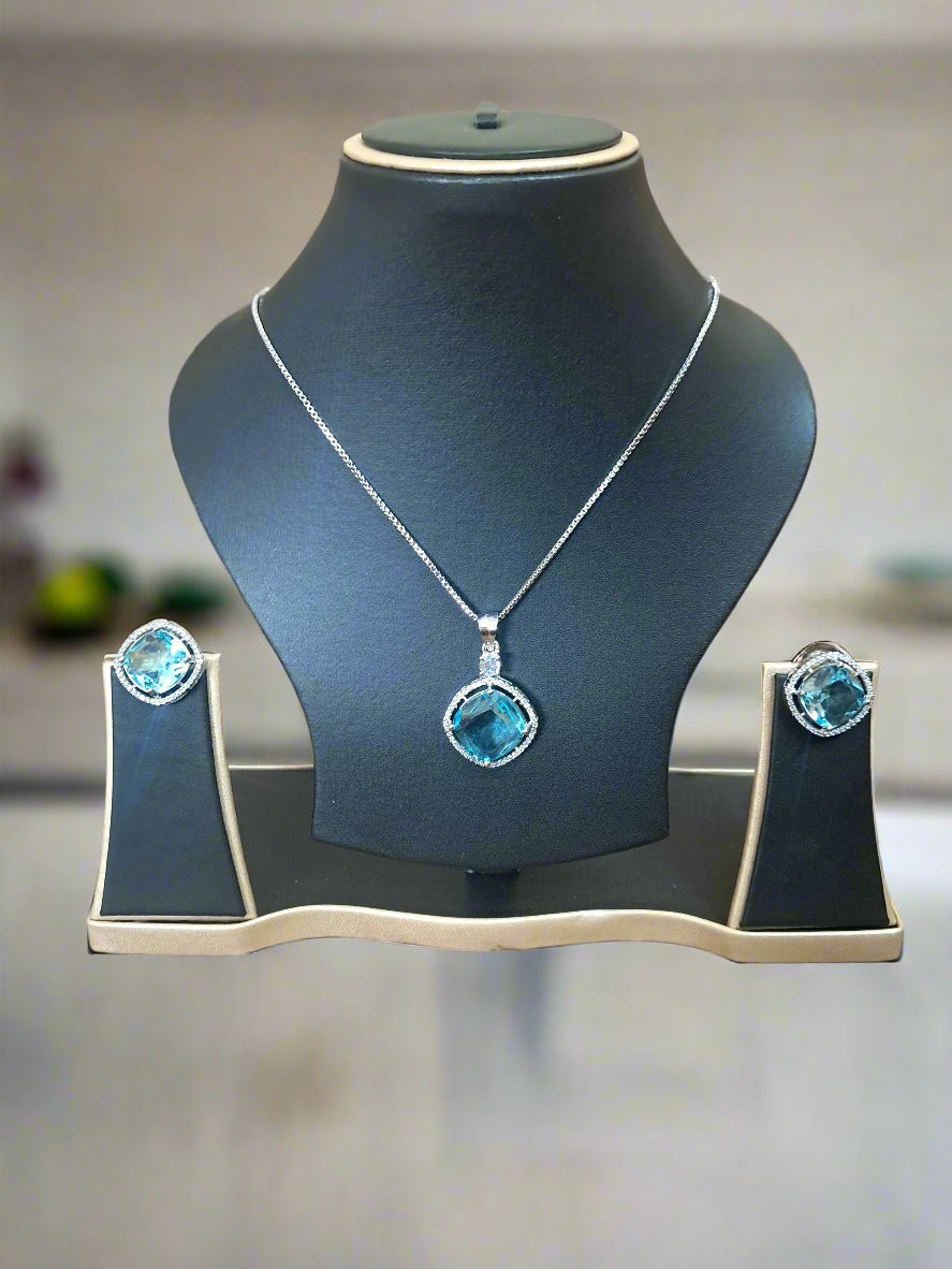 rn-image_picker_lib_temp_2f7017d5-4468-488d-b366-859b28696b1c-1 Aqua Blue Pendant Set with CZ studs and silver-plated chain displayed elegantly on a jewelry stand.